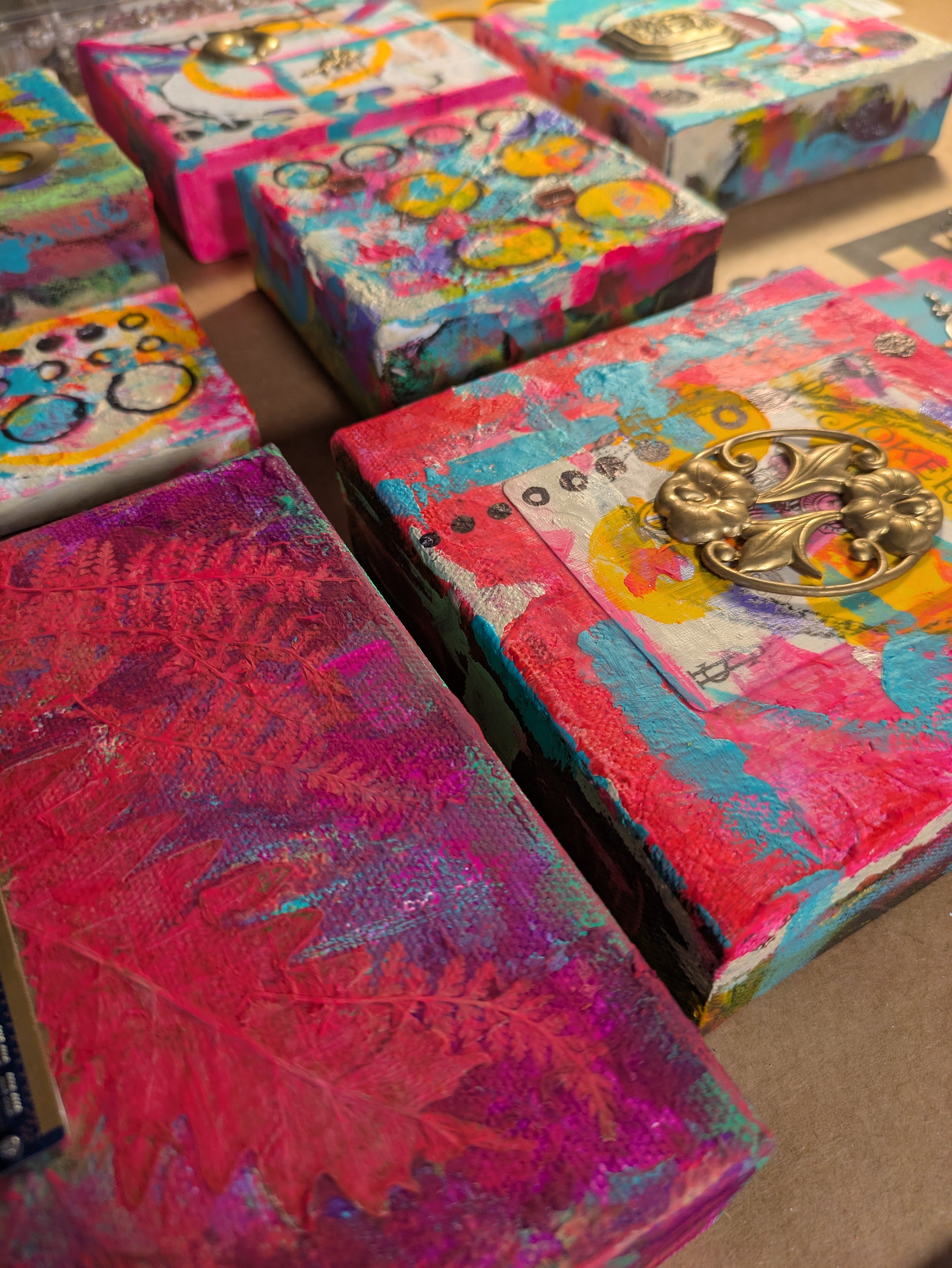 Colorful paintings on canvas with eclectic patterns and gold accents on a flat surface.