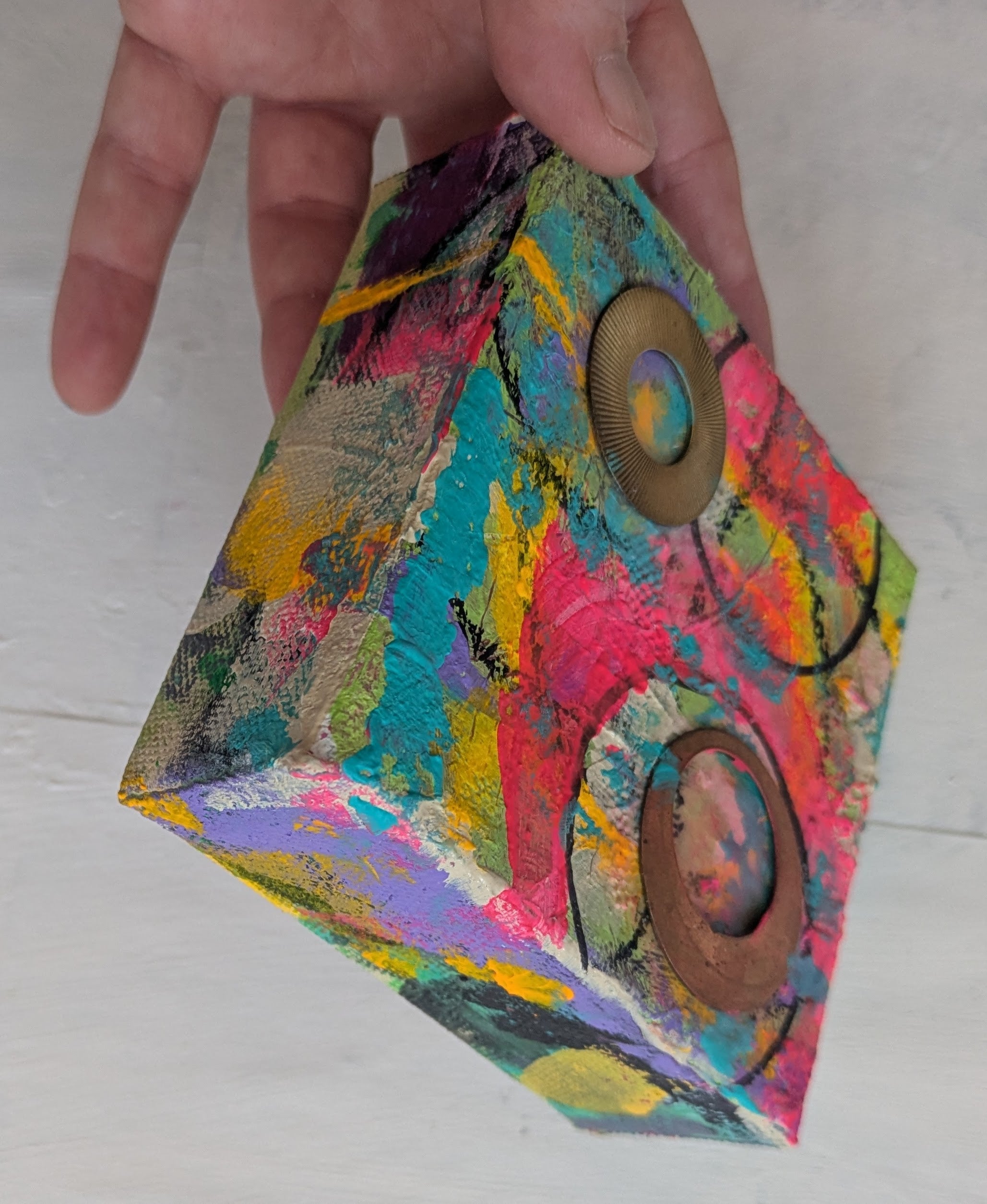 Colorful textured painting on canvas with circular designs held by a hand on a white background